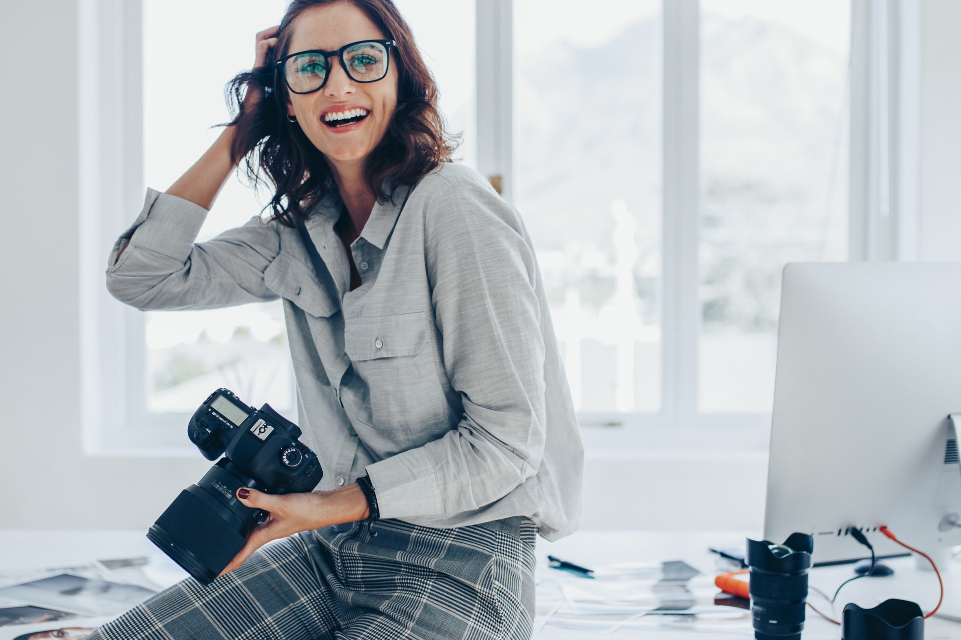 Mujer sonriente vestida en tonos grises soteniendo con una mano una cámara fotográfica reflex como ejemplo del máster en comunicación de moda de INNADI, Madrid.